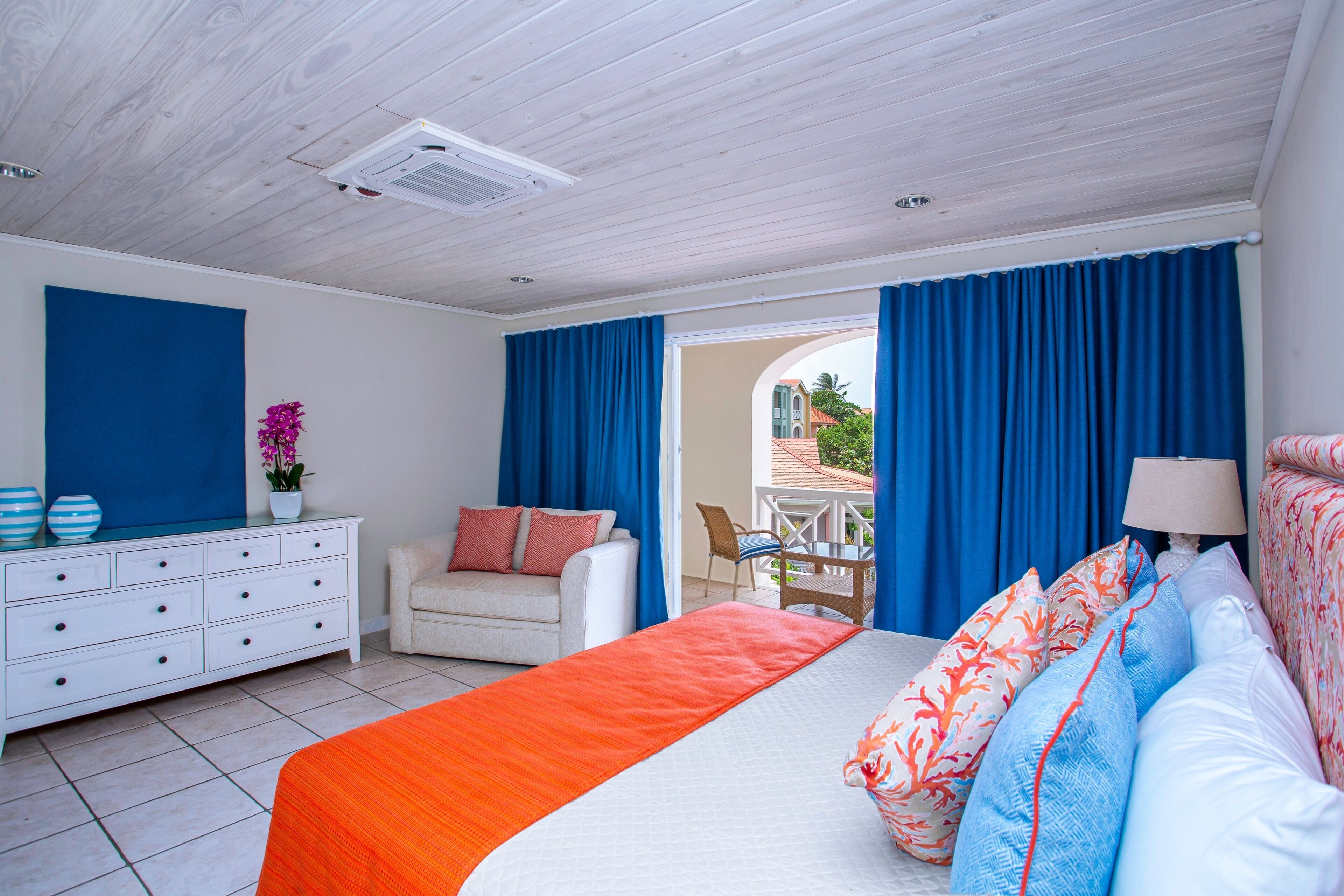 A bedroom with a bed, a dresser, a chair, and a view of the outside.