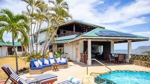 Una casa de dos pisos con piscina, mobiliario exterior y vista al océano.