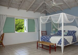 Un dormitorio con cama con dosel, un banco de madera, una silla y un ventanal con contraventanas verdes.
