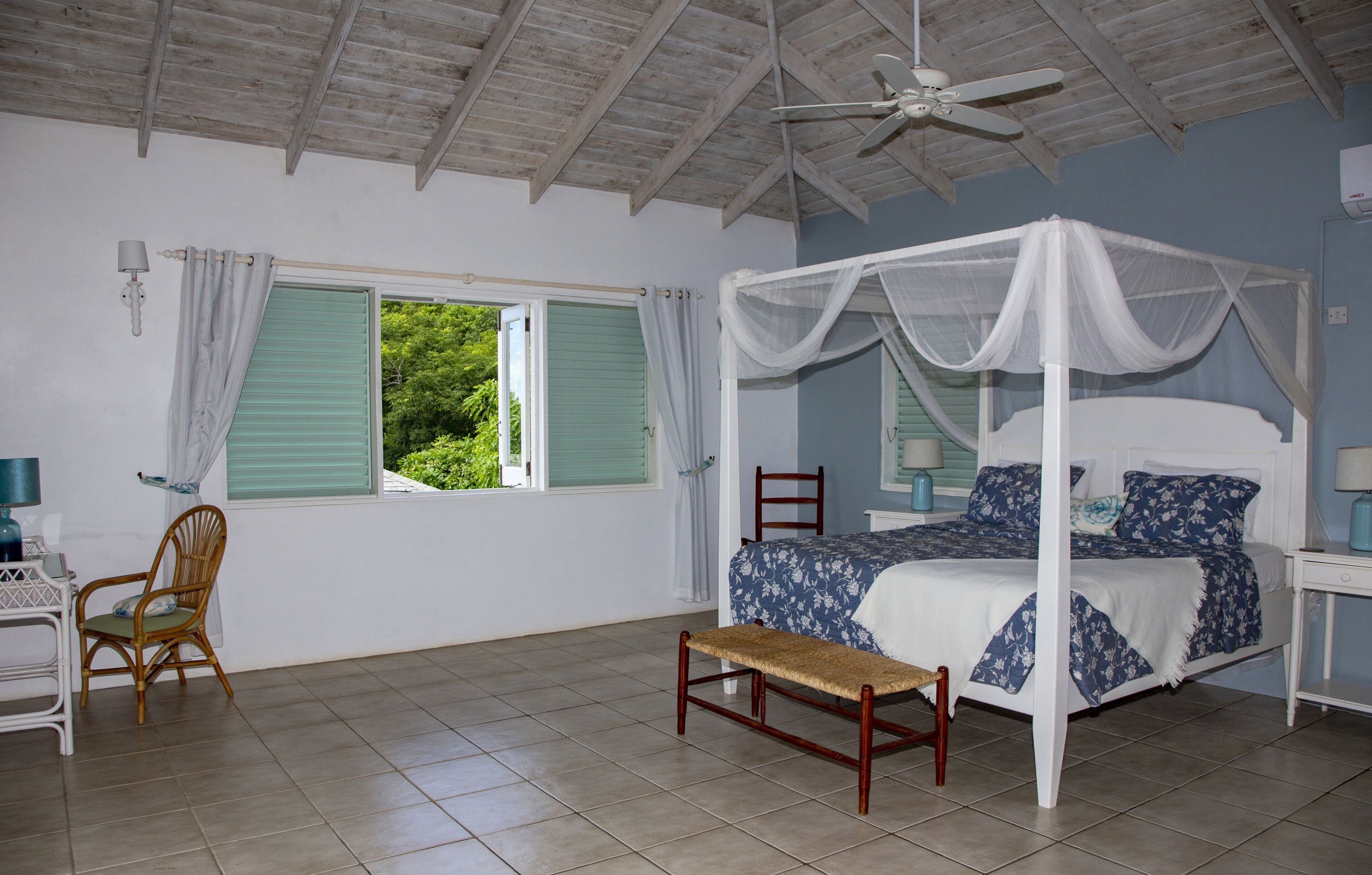 A bedroom with a four-poster bed, a chair, a small table, and a ceiling fan.
