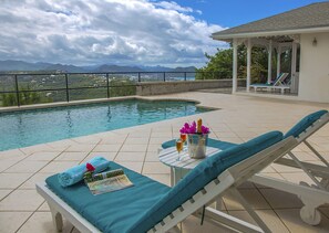 Zona de piscina con vistas a montañas, un espacio de descanso cubierto y una mesa con una botella y vasos.