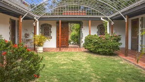 A covered patio with a glass ceiling, a wooden door, and a small garden area with red flowers and green shrubs. - Spanish-style Ocean View Villa Set In Garden - Calypso Court 3 Bedroom Villa by RedAwning (Gros Islet)