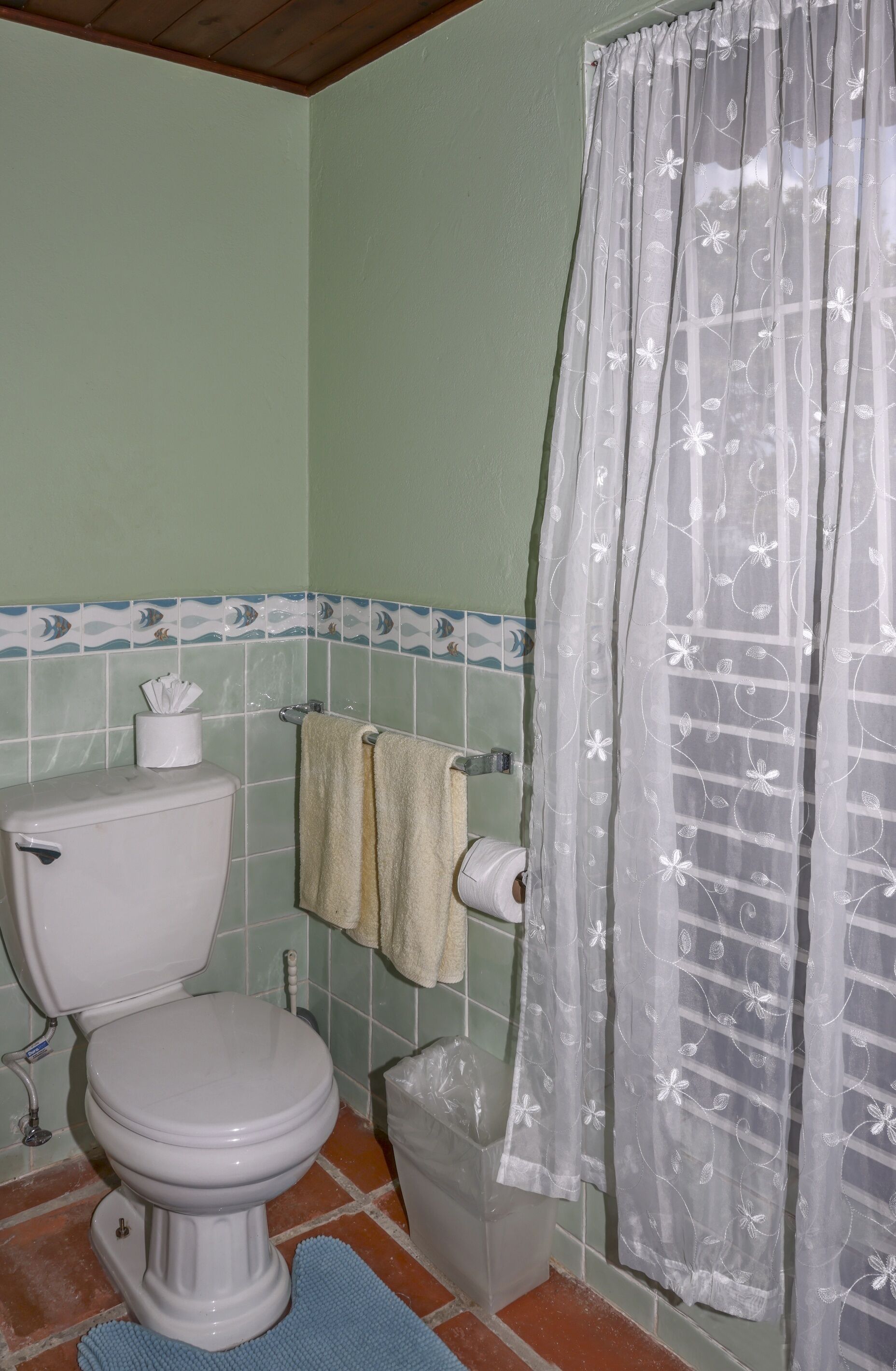 A bathroom with a toilet, a towel rack, a shower curtain, and a trash bin.