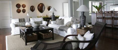 A living room with a sofa set, coffee table, and armchair, with decorative wall art and a dining area in the background.