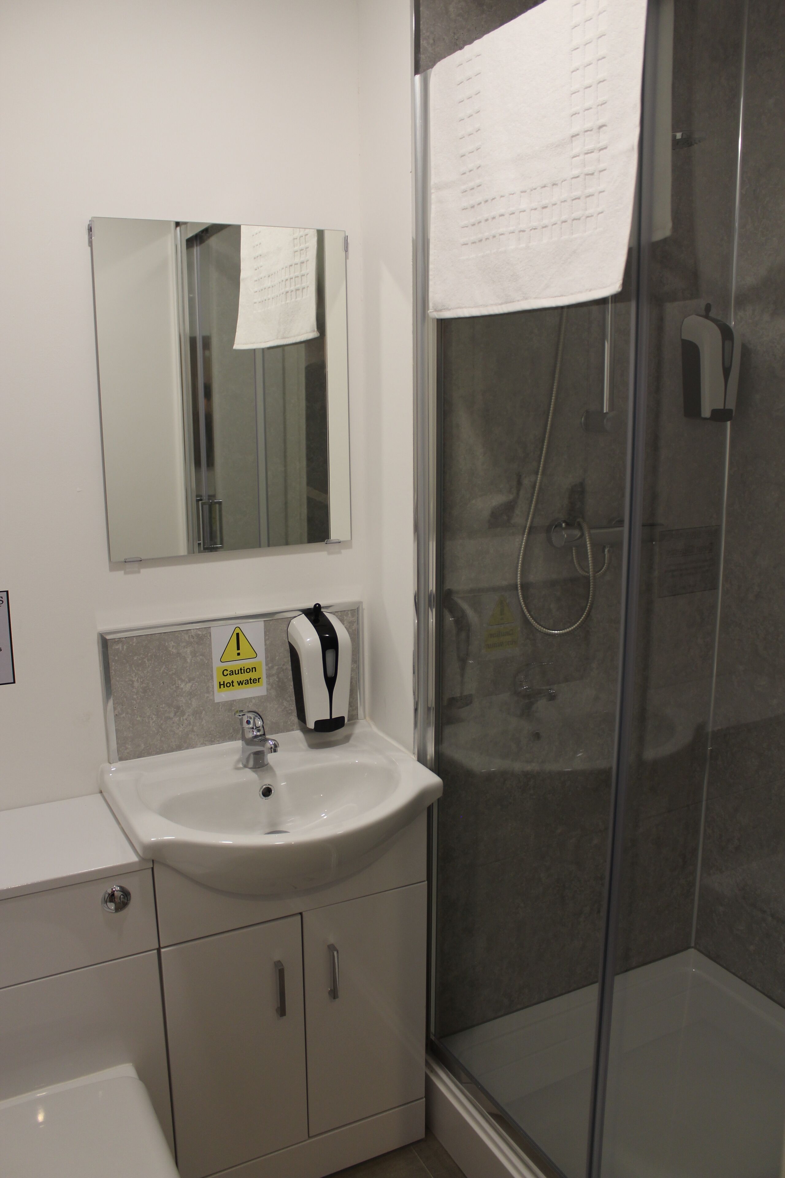 A bathroom with a sink, mirror, caution sign, and a glass shower enclosure.