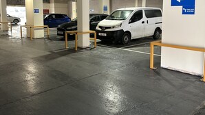 Un parking souterrain où sont garées plusieurs voitures, dont un fourgon blanc et une voiture bleue, ainsi qu’un panneau de signalisation indiquant qu’il s’agit d’une voie à sens unique.