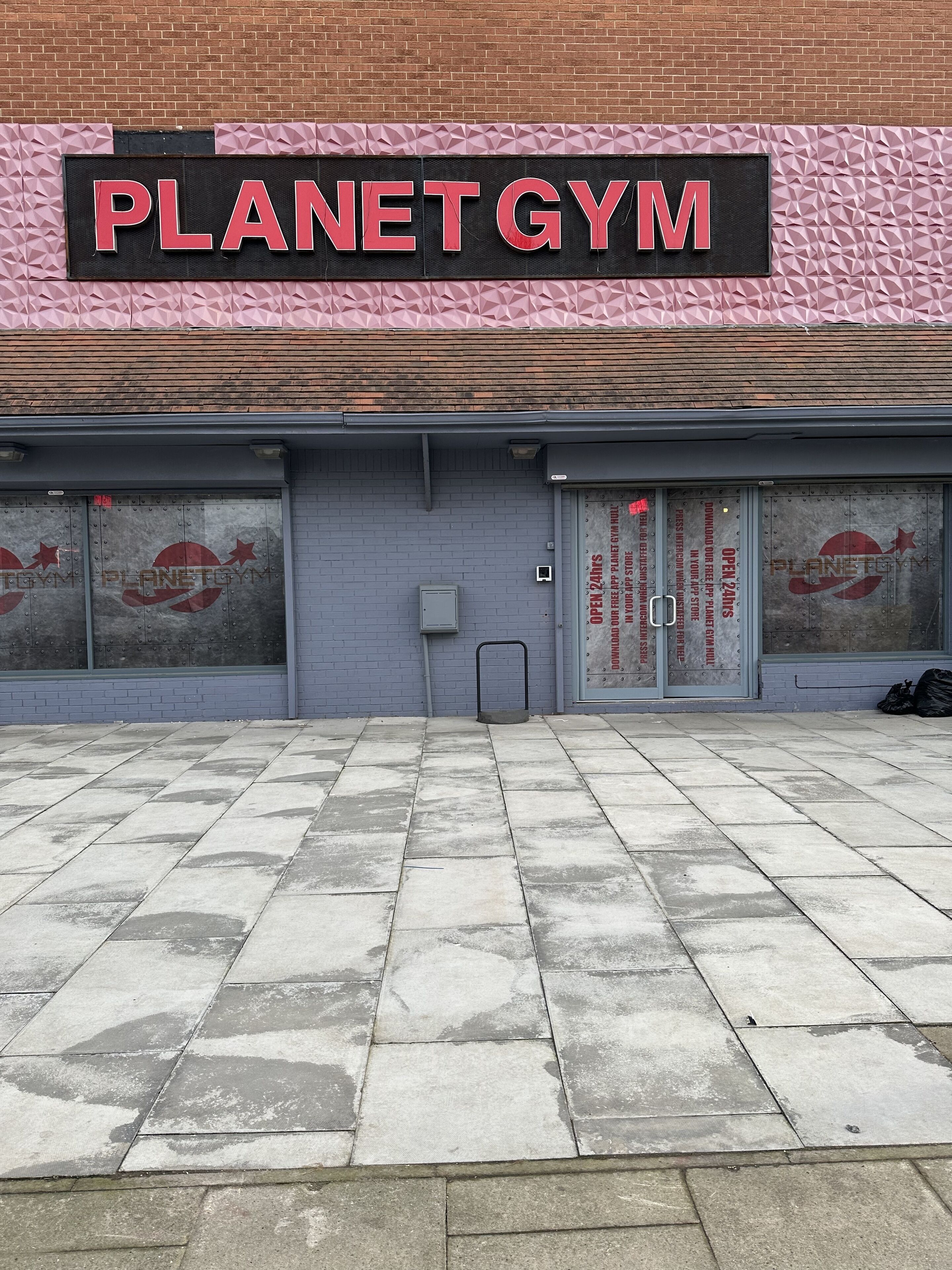 Ein Planet Gym mit Ziegelaußenwand, großen Fenstern und einem gefliesten Eingangsbereich.