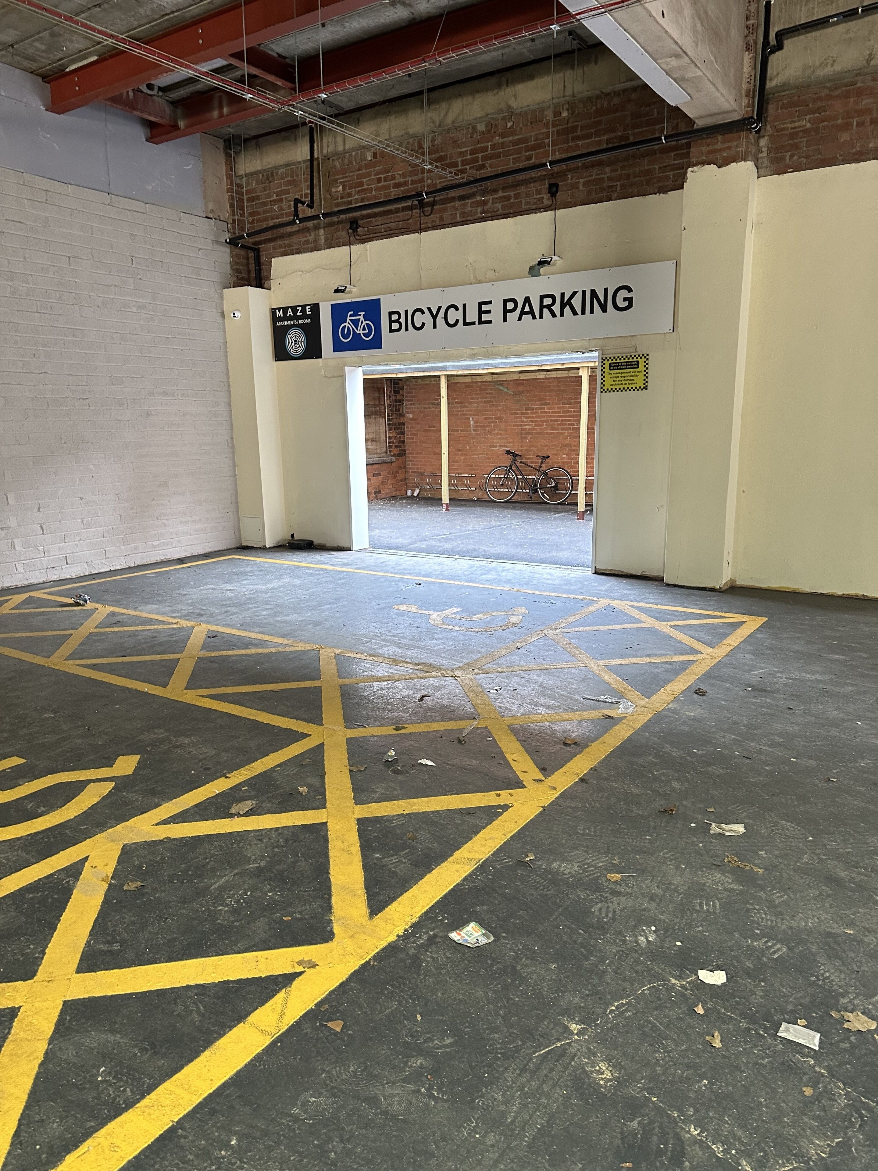 Een fietsenparkeerplaats met een bord waarop staat dat het voor fietsen is, een bakstenen muur en een betonnen vloer met gele markeringen.