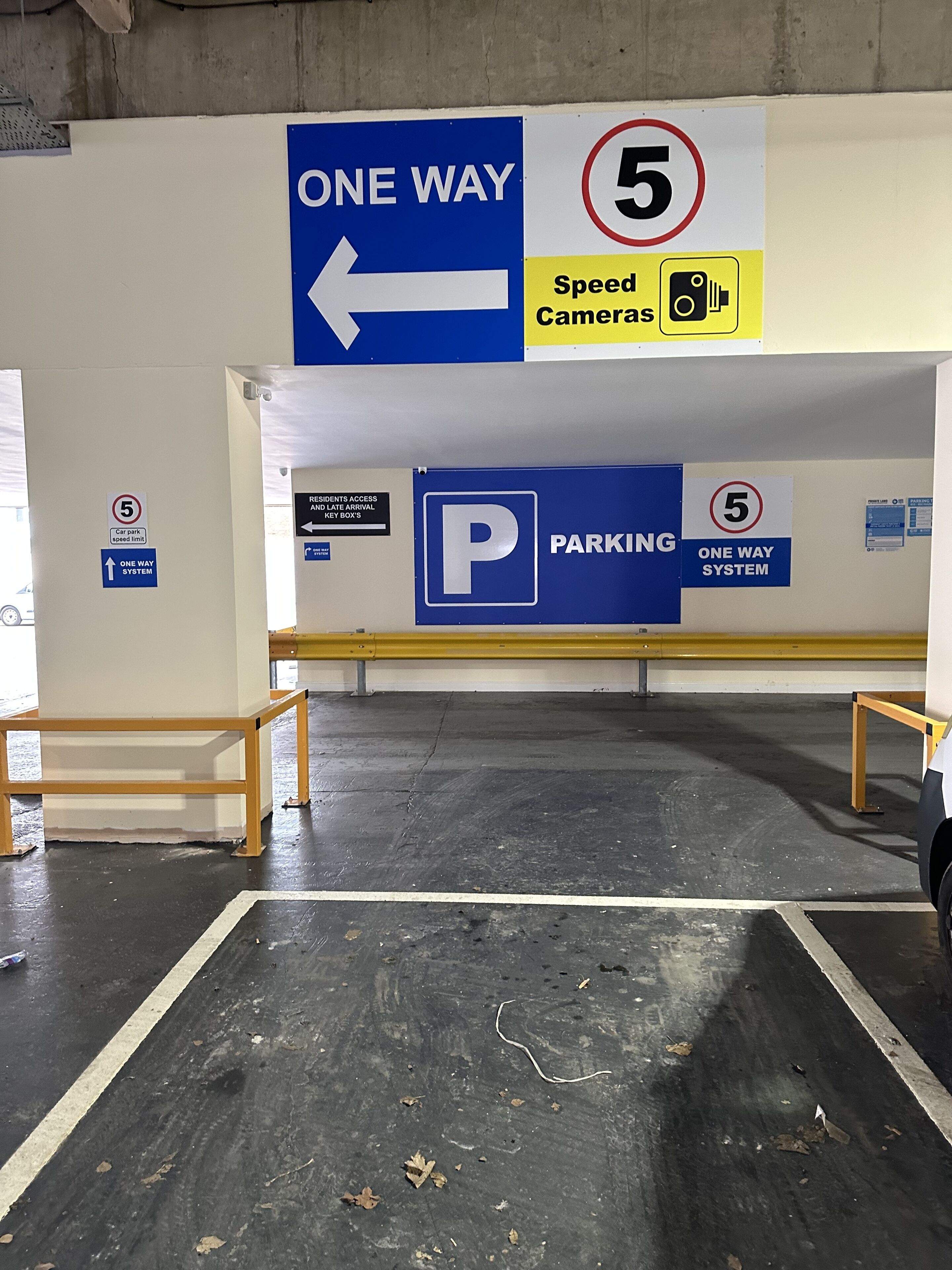 A parking garage with one-way signs, speed limit signs, and a speed camera warning.