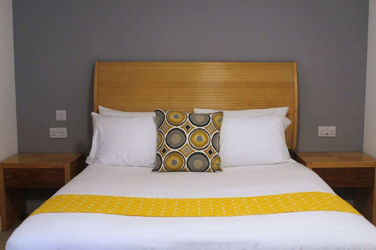 A bed with a wooden headboard, white and yellow bedding, and a patterned pillow.