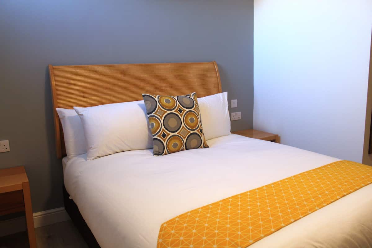 A neatly made bed with a wooden headboard, white bedding, and a patterned throw blanket.