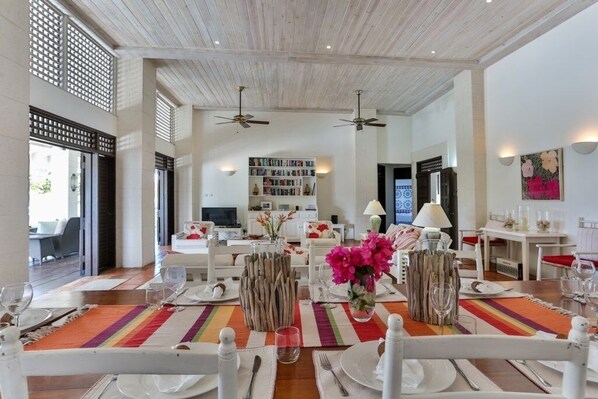 A dining area with a long table set for a meal, a bookshelf in the background, and a ceiling fan.