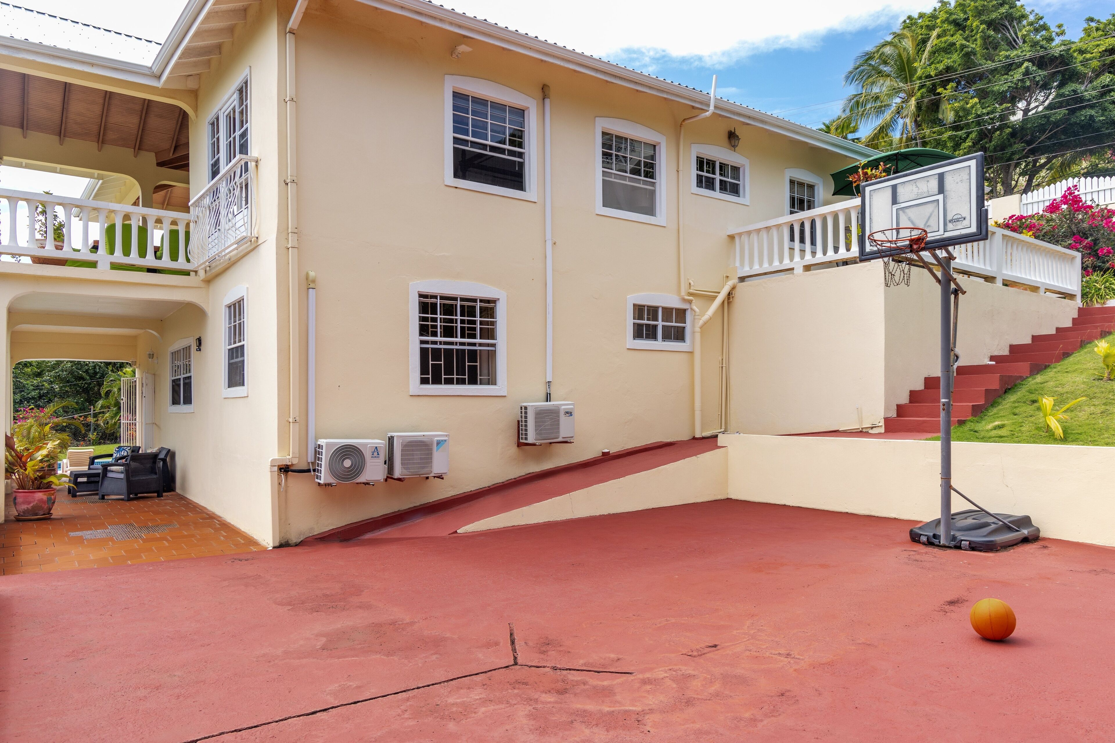 Una casa de dos pisos con un aro de baloncesto, un porche cubierto y una escalera que lleva al piso superior.