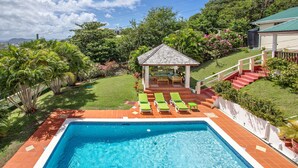 Una piscina con solárium de baldosas, un pabellón y mobiliario exterior.