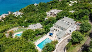 An aerial view of a residential area with multiple houses, a swimming pool, and a view of the ocean.