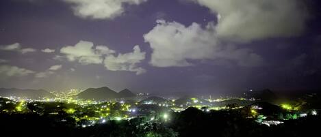 A nighttime cityscape with illuminated buildings and mountains in the background.