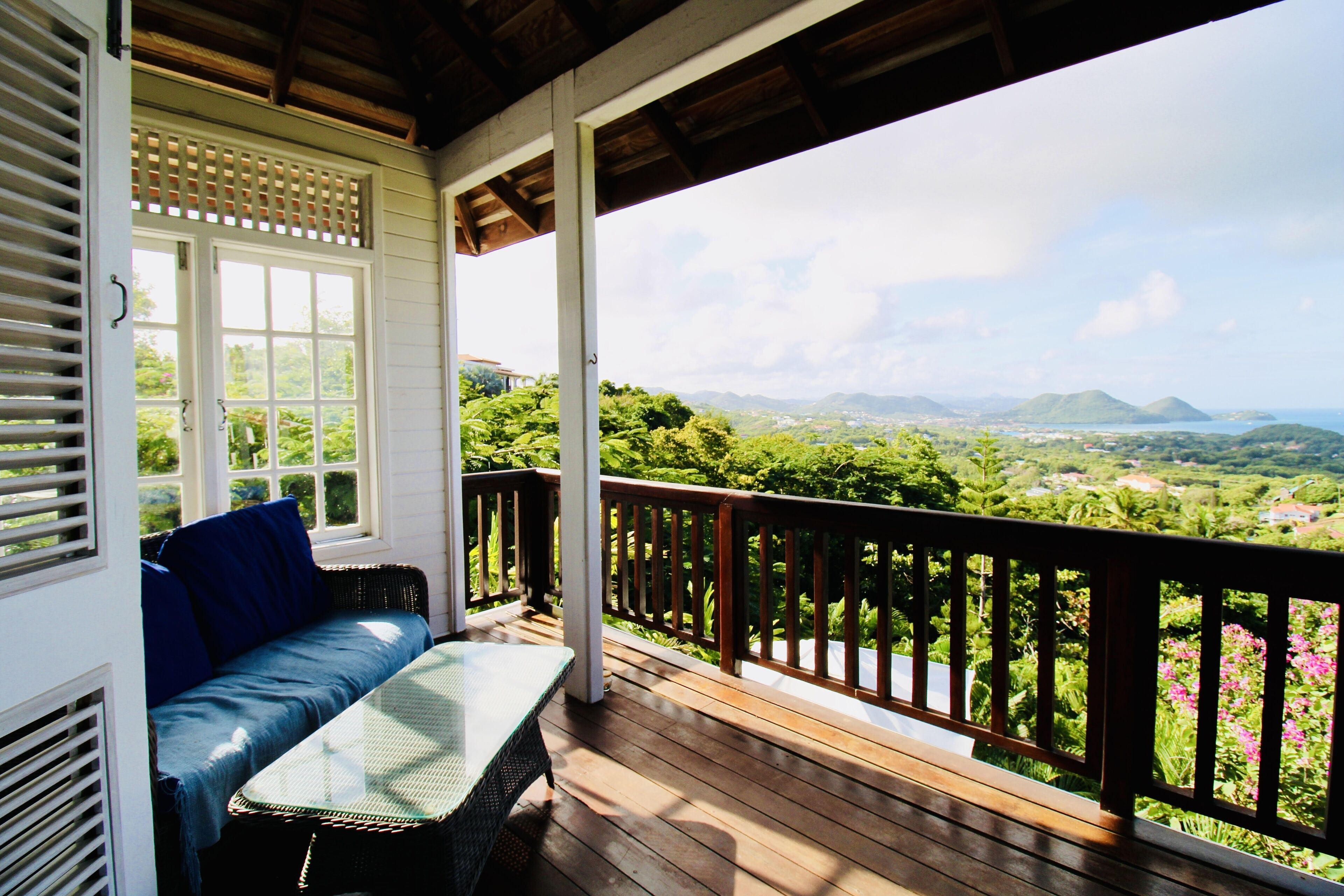 A covered porch with a wooden deck, a cushioned bench, and a table.