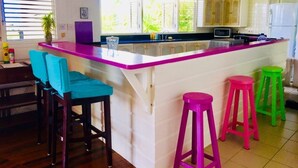Une cuisine dotée d’un îlot central, de meubles de rangement en bois et de tabourets colorés.