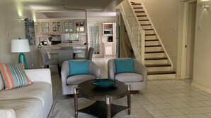 A living room with a sofa, two armchairs, a coffee table, and a staircase. - Bay View #7 - 3 bedroom, 3.5-bath waterfront townhouse in a gated community in Rodney Bay 3 Townhouse by RedAwning (Gros Islet)