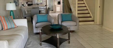 A living room with a sofa, two armchairs, a coffee table, and a staircase.