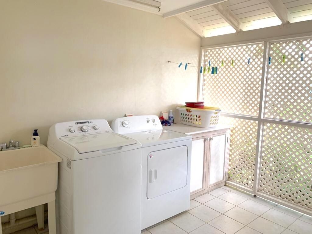 A laundry room with a washing machine, dryer, and a sink. There is a window with a lattice screen and a door with a handle.