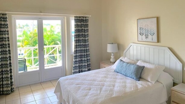 A bedroom with a bed, a nightstand, a lamp, and a view through a sliding door to an outdoor area with greenery. - Bay View #7 - 3 bedroom, 3.5-bath waterfront townhouse in a gated community in Rodney Bay 3 Townhouse by RedAwning (Gros Islet)