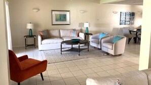A living room with a white sofa, a teal armchair, and a red chair. There are two side tables with lamps, a ceiling fan, and a framed picture on the wall. - Bay View #7 - 3 bedroom, 3.5-bath waterfront townhouse in a gated community in Rodney Bay 3 Townhouse by RedAwning (Gros Islet)
