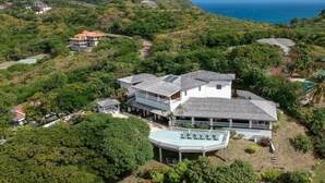 A large, multi-story house with a spacious patio area, surrounded by lush greenery and overlooking a coastal view. - Sprawling three bedroom villa - Tamarind Villa 3 Villa by RedAwning (Gros Islet)