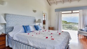 A bedroom with a bed, a nightstand, a lamp, a chair, and a balcony with a view. - Sprawling three bedroom villa - Tamarind Villa 3 Villa by RedAwning (Gros Islet)