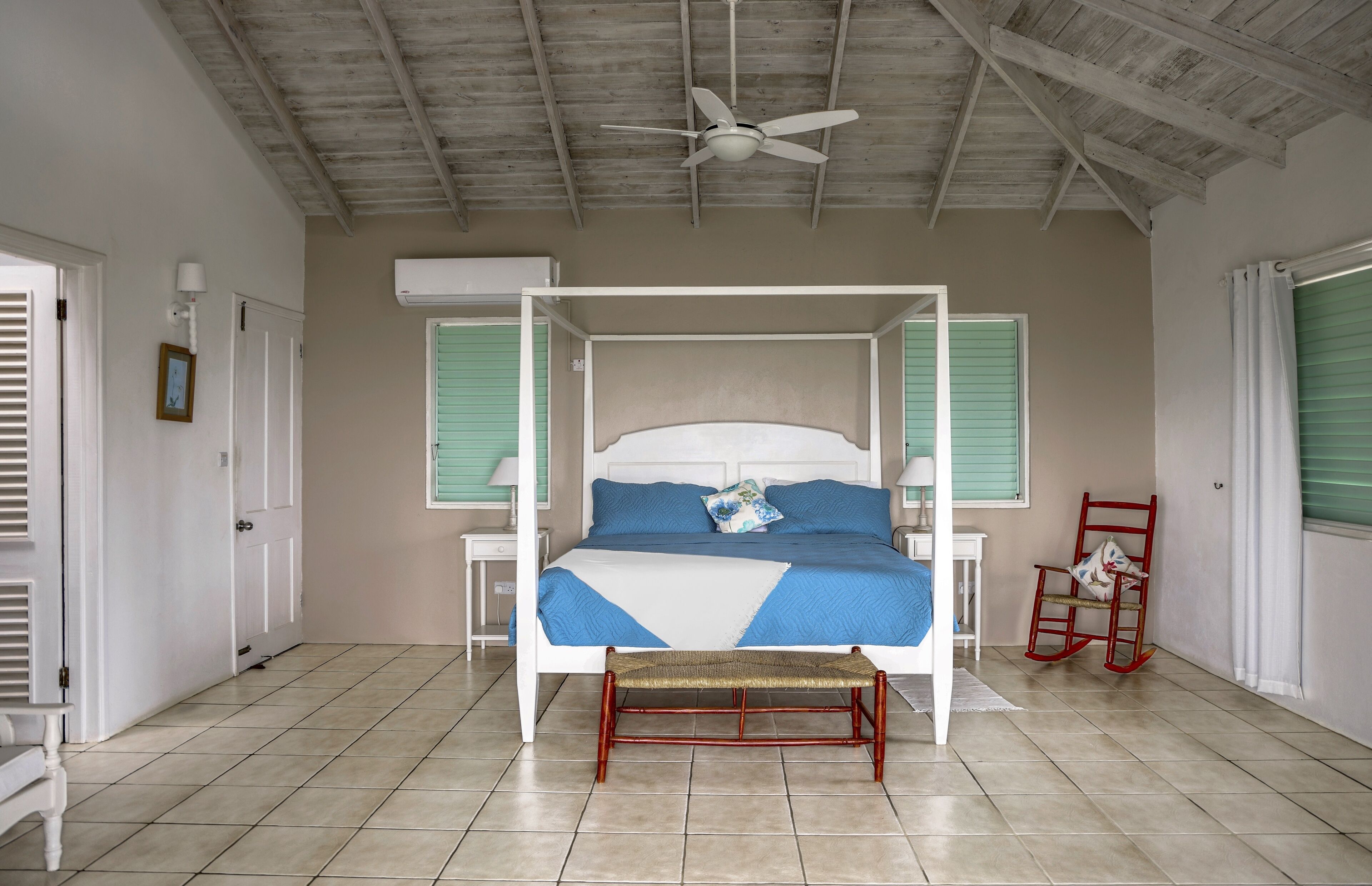 A spacious bedroom with a four-poster bed, a ceiling fan, and a rocking chair.