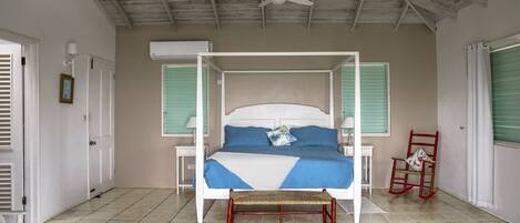 A spacious bedroom with a four-poster bed, a ceiling fan, and a rocking chair.