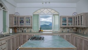 A kitchen with a central island, wooden cabinets, and a view of mountains through a window. - Zephyr Hill - 2 bedroom Villa with awe inspiring views 2 Villa by RedAwning (Gros Islet)