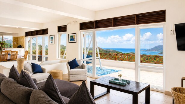 A spacious living room with a large sofa, a coffee table, and a view of the ocean through large sliding doors. - Hilltop Villa With Great Views Out To Sea - Villa Cadasse 3 Bedroom Villa by RedAwning (Gros Islet)