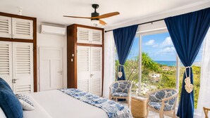 A bedroom with a bed, two chairs, a ceiling fan, and a view of the sea. - Hilltop Villa With Great Views Out To Sea - Villa Cadasse 3 Bedroom Villa by RedAwning (Gros Islet)