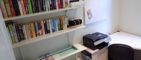 Een werkplek aan huis met een bureau, stoel en boekenplanken vol boeken.