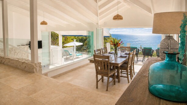 Un'ampia sala da pranzo con vista sull'oceano, una scala in pietra e un grande vaso decorativo.