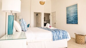 Una camera d'hotel con un letto, una ventola a soffitto, un quadro raffigurante il mare e un cesto in vimini.