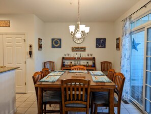 Un comedor con una mesa de madera, sillas, una lámpara de araña y una ventana con cortinas.
