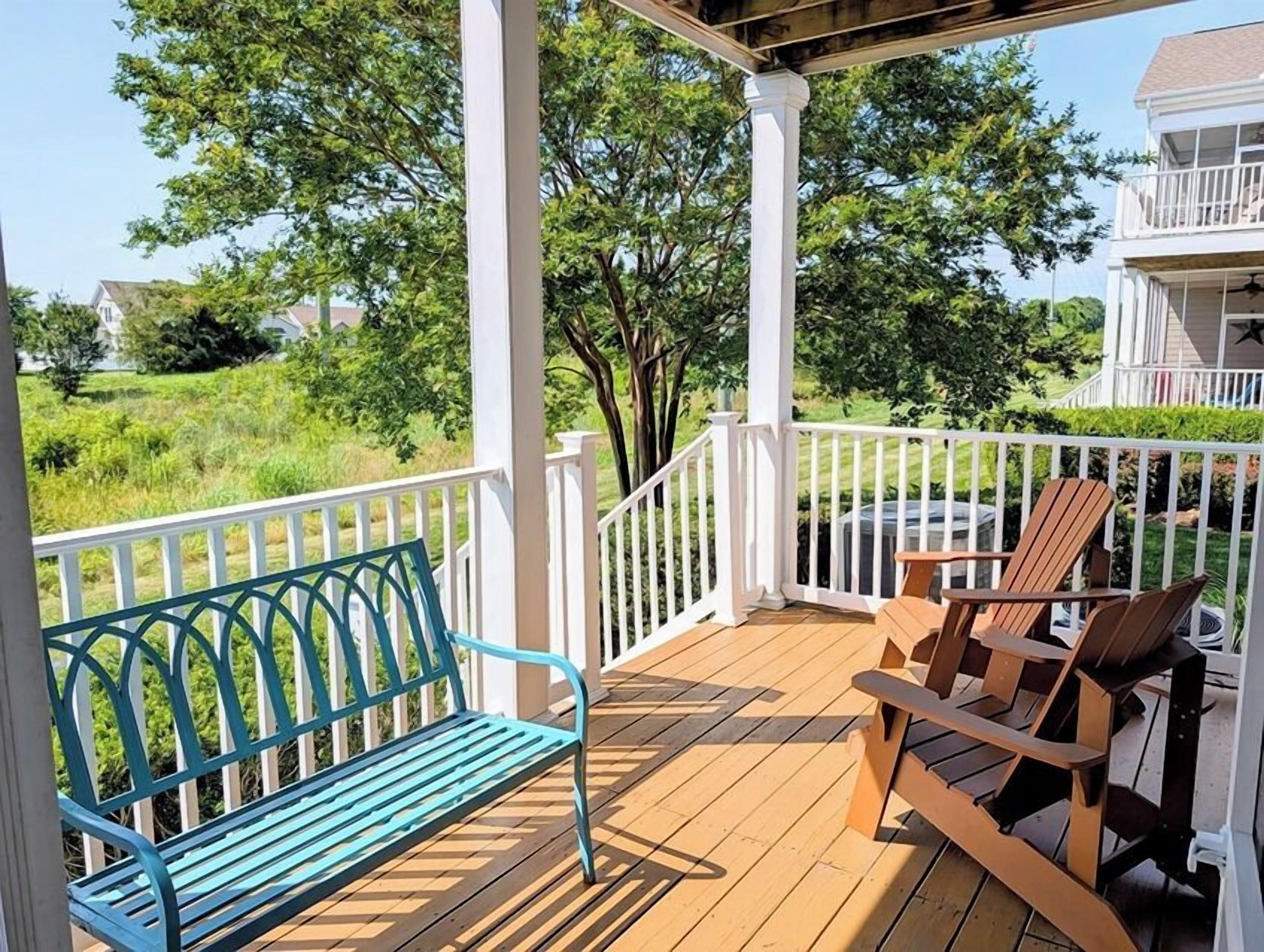 A wooden deck with a bench and chairs, surrounded by white railings.