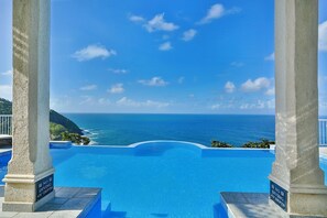 A infinity pool with a view of the ocean, surrounded by white columns and a clear blue sky.