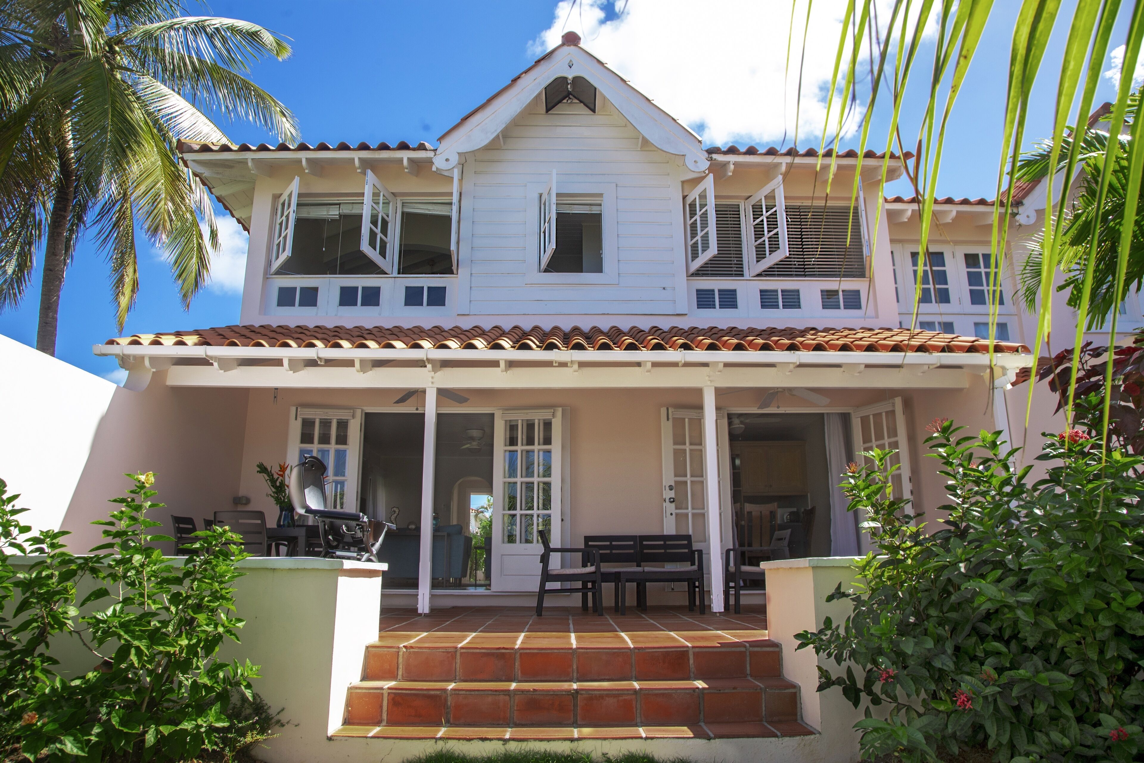 Una casa de dos pisos con un porche, una escalera que conduce a la entrada y un patio con mobiliario exterior.