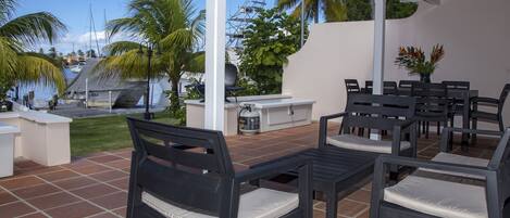 Un patio al aire libre con una parrilla, zona de estar y vistas al puerto deportivo.