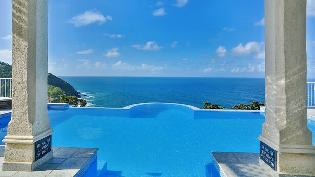 A infinity pool with a view of the ocean, surrounded by white columns and a clear blue sky. - Cayman Villa - Contemporary 4 bedroom Villa with Stunning Ocean Views 4 Villa by RedAwning (Gros Islet)