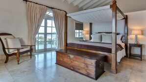 A spacious bedroom with a four-poster bed, a wooden bench, a nightstand, and a chair. - Cayman Villa - Contemporary 4 bedroom Villa with Stunning Ocean Views 4 Villa by RedAwning (Gros Islet)