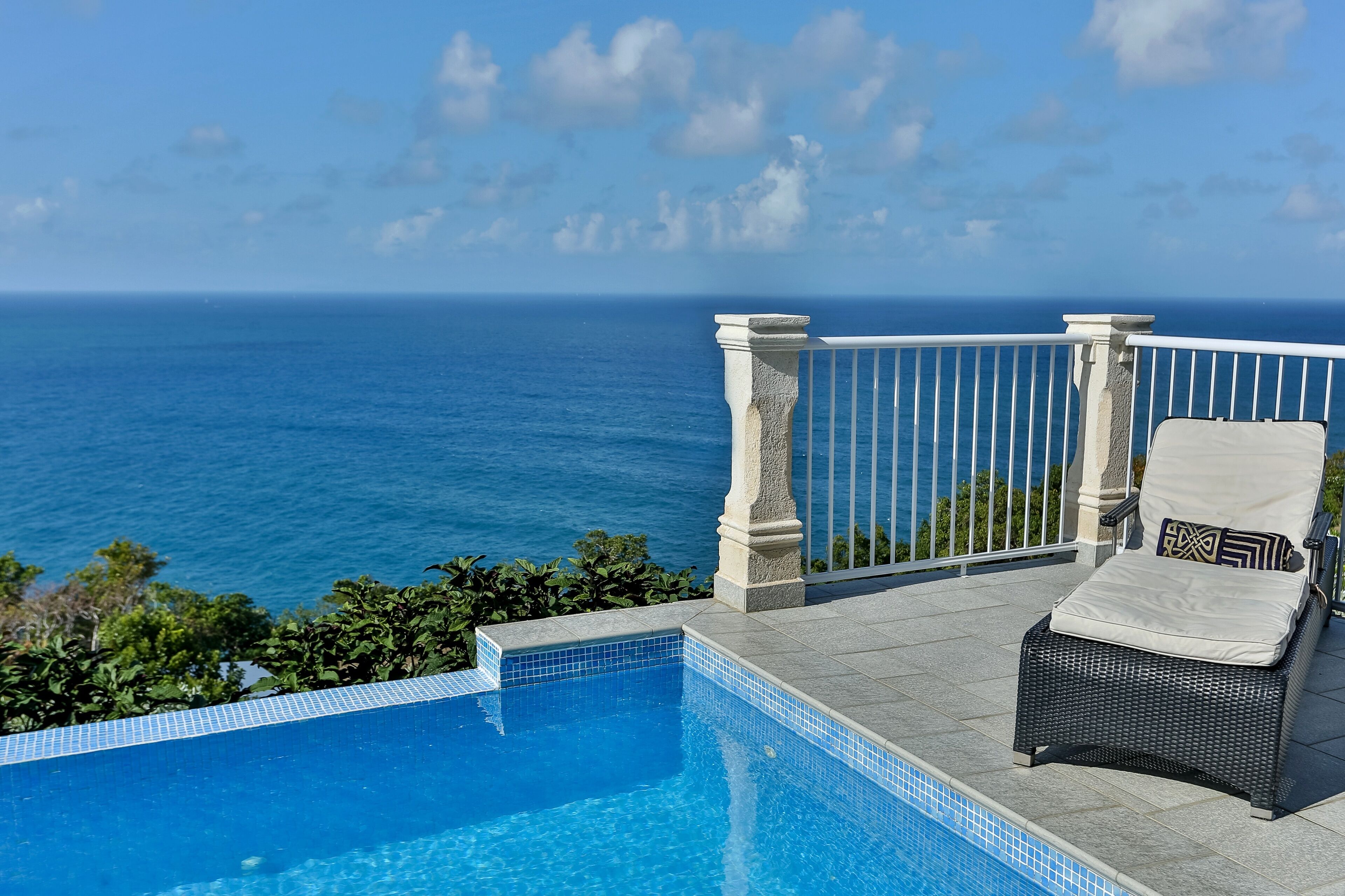 A poolside area with a view of the ocean, a lounge chair, and a tiled pool.