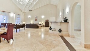 A spacious living area with a high ceiling, a dining area with red chairs, and a fireplace. - Cayman Villa - Contemporary 4 bedroom Villa with Stunning Ocean Views 4 Villa by RedAwning (Gros Islet)