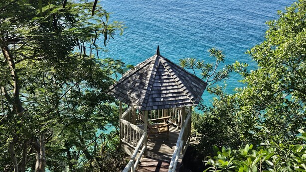 A wooden gazebo with a thatched roof overlooking a body of water, surrounded by dense foliage. - Smuggler's Nest - Exotic & Romantic Villa 2 Bedroom Villa by RedAwning (Gros Islet)