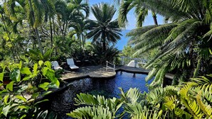 A tropical pool surrounded by lush greenery and palm trees, with lounge chairs and a small bridge. - Smuggler's Nest - Exotic & Romantic Villa 2 Bedroom Villa by RedAwning (Gros Islet)