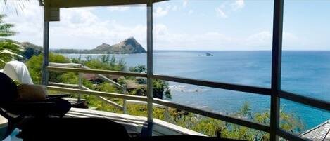 A room with a large window overlooking a coastal view, including a mountain and the sea.