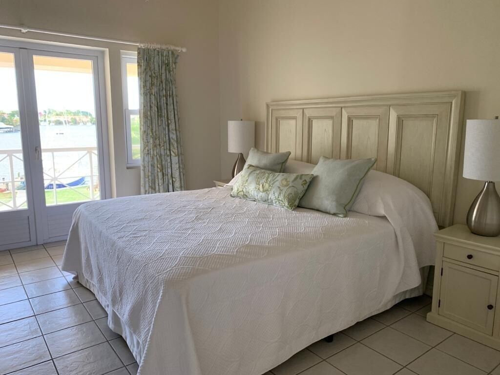 A bedroom with a large bed, two bedside lamps, a nightstand, and a view through a glass door to an outdoor area.
